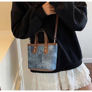 Detail of denim crossbody bag with brown leather handles and metallic studs shown on model