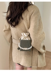 Detail of dark green retro square bag with pearl handle and metal chain on beige coat