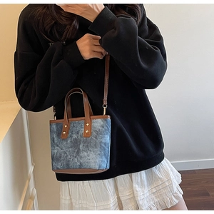 Detail of blue denim mini tote with brown leather straps and gold rivet accents