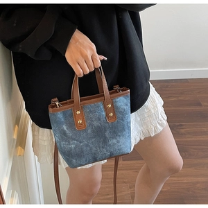 Détail du sac seau vintage en denim bleu avec poignée en cuir marron et rivets dorés