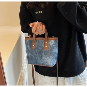 Detail view of blue denim mini tote bag with brown leather trim and golden rivets
