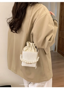 Detail of white textured mini bag featuring pearl bead handle and golden chain strap