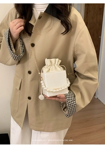 Close-up of a white square bucket bag with pearl handle and golden chain strap detail