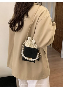 Detail of minimalist bucket bag with pearl handle and golden chain on a model