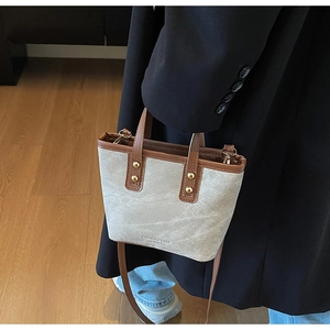 Detail of mini canvas bucket bag with brown leather trim and gold rivet accents