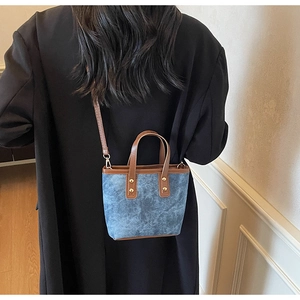 Fashion denim bucket bag with brown leather straps worn over the shoulder by a model