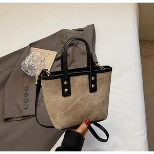 Detail of canvas bucket bag with black leather trim and gold studs in lifestyle setting