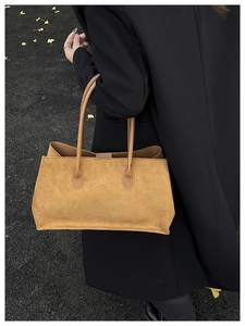 Grand sac cabas en daim marron porté avec un manteau noir dans un décor d'automne