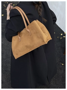 Close-up of a large brown suede tote bag carried over the shoulder of a black coat
