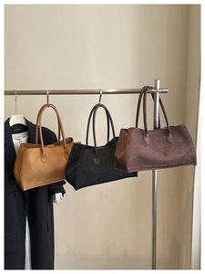 Three suede tote bags in caramel, black and dark brown hanging for storage display