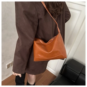 Close-up of caramel brown leather tote bag with glossy finish on a minimalist model