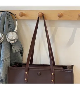 Detail of dark brown leather tote bag with gold rivets hanging on a wooden hook