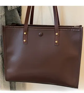 Detail of dark brown leather tote bag showing soft texture and golden rivet accents