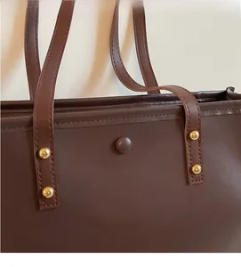 Close-up of vintage dark brown leather tote bag with gold rivets and magnetic buckle