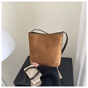 Close-up of a brown suede bucket bag with long shoulder strap and minimalist texture