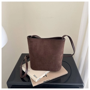 Detailed view of dark brown suede bucket bag texture on minimalist cream background
