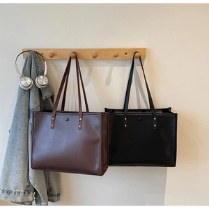 Detail view of large retro tote bags in black and brown hanging on a wooden rack