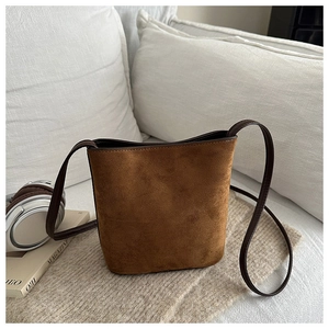 Detailed macro view of a brown suede bucket bag with leather strap on a soft blanket