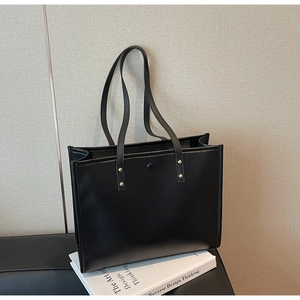 Detail view of large black matte tote bag with gold rivets on a decorative book