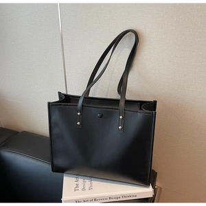 Close-up of minimalist black leather tote bag with gold studs on a leather sofa