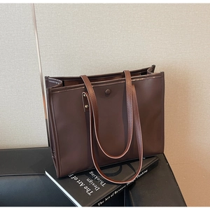 Detail of dark brown tote bag with thin shoulder straps and golden rivet accents