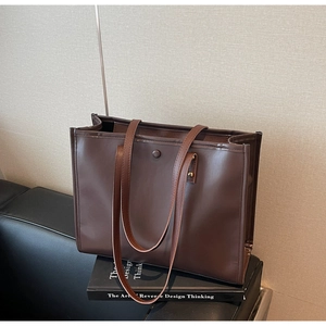 Close-up of a vintage brown leather tote bag resting on a book in a minimalist setting