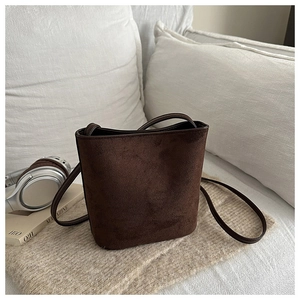 Detail of dark brown matte suede bucket bag with long strap on soft home decor