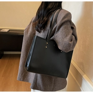Detail of black leather tote bag featuring gold rivet studs and sturdy shoulder straps
