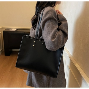 Detail of minimalist black PU leather tote bag with elegant gold rivet accents and long straps