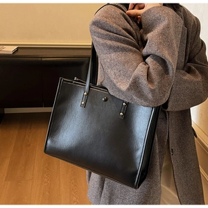 Close-up of black vintage leather tote bag with gold stud hardware on shoulder straps
