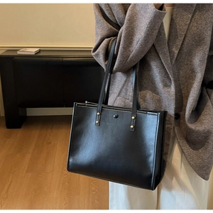 Detail view of a large black vintage tote bag with gold rivets and shiny PU leather finish
