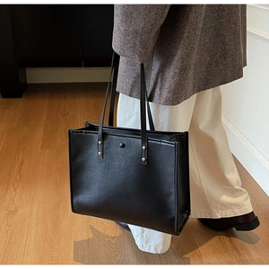 Detailed side view of a black leather tote bag with gold rivets on a model