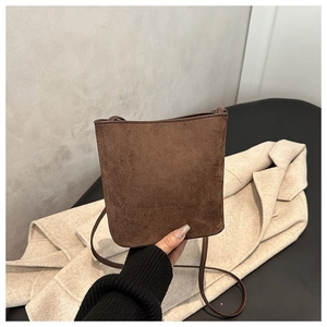 Detailed close-up of dark brown suede bucket bag with fine stitching and slim shoulder strap