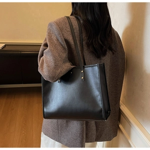 Model wearing a minimalist black leather tote bag with gold rivets in daily scene