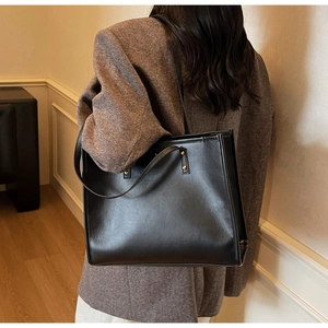 Model wearing a large black leather tote bag with fine texture and metal studs detail