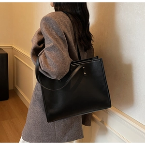 Detail of a large vintage black faux leather tote bag worn by a model in a blazer