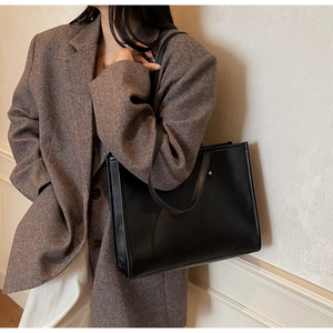 Side view of a large black matte leather tote bag worn by a model in a brown blazer
