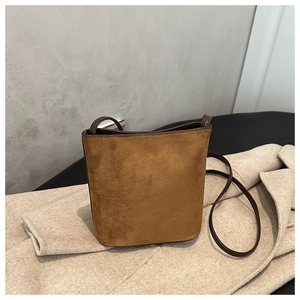 Detail of a brown suede bucket bag with leather piping on a warm wool coat background