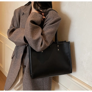 Detail of a black large capacity tote bag with gold rivets on shoulder straps