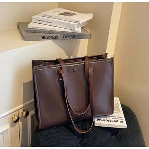 Detailed view of deep brown vintage leather tote bag with magnetic clasp on a sofa