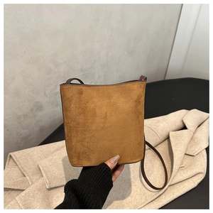 Detail view of a tan suede bucket bag with dark brown leather piping and shoulder strap