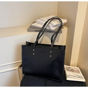 Detail of minimalist black tote bag with long shoulder straps and gold rivet hardware