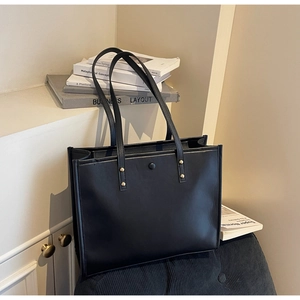 Detail of black leather tote bag with gold rivet accents and magnetic snap closure