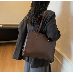 Detail shot of a dark brown matte leather tote bag with vintage gold metal rivets