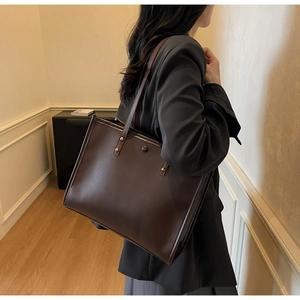 Deep brown matte leather tote bag worn by a model in a cozy indoor home setting