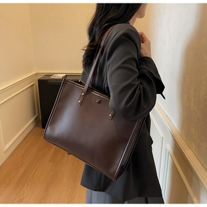 Detail view of deep brown faux leather tote bag showing smooth matte texture and rivets