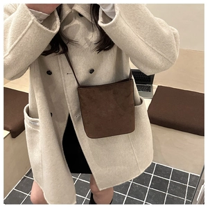 Detail view of dark brown suede bucket bag worn with a stylish cream wool coat