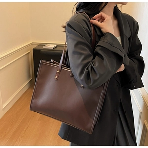 Detail view of large dark brown leather tote bag showing side seams and metal rivet accents