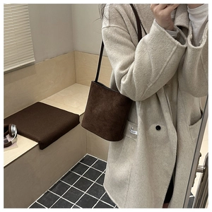Detail of dark brown suede bucket bag worn by model in a cozy indoor lifestyle setting