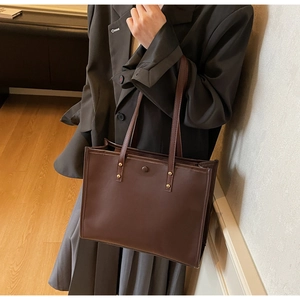 Retro dark brown leather tote bag with gold studs worn over the shoulder for commute
